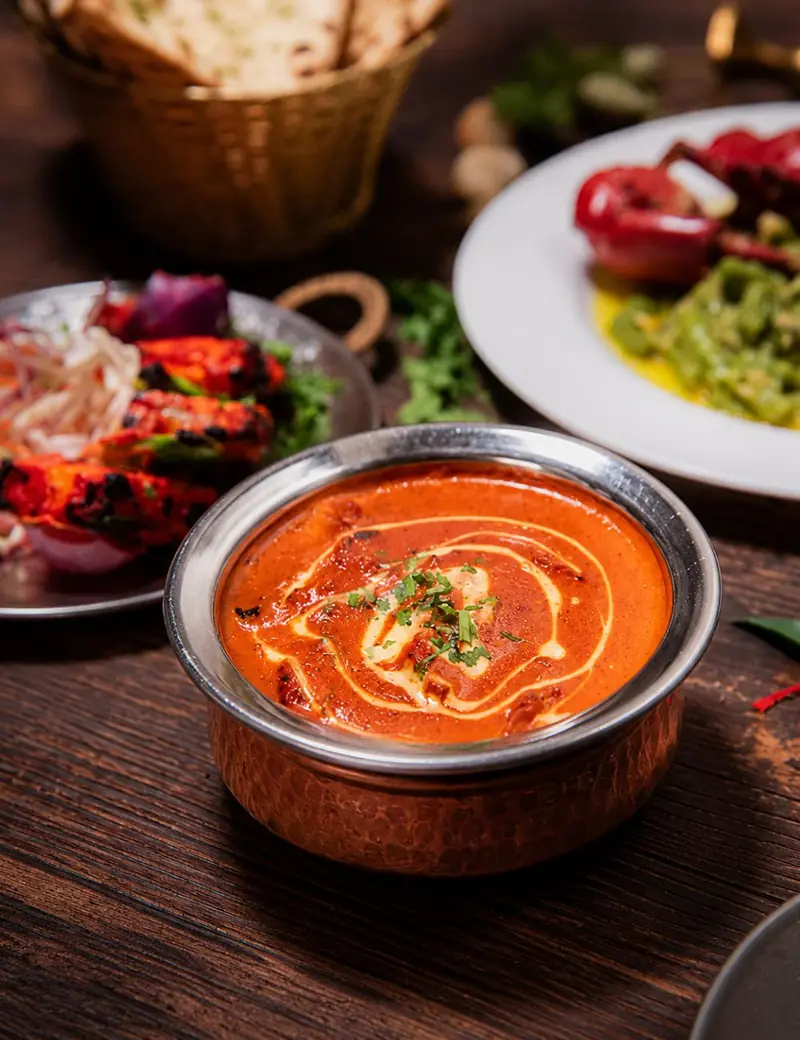 Butter chicken in a copper bowl, with tandoori chicken and naan on the table