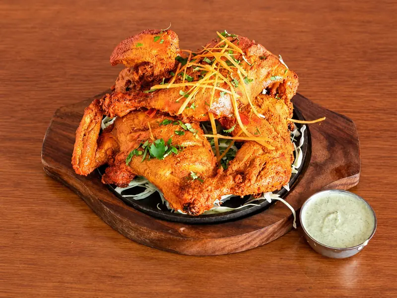 Tandoori chicken on a sizzler plate with mint chutney